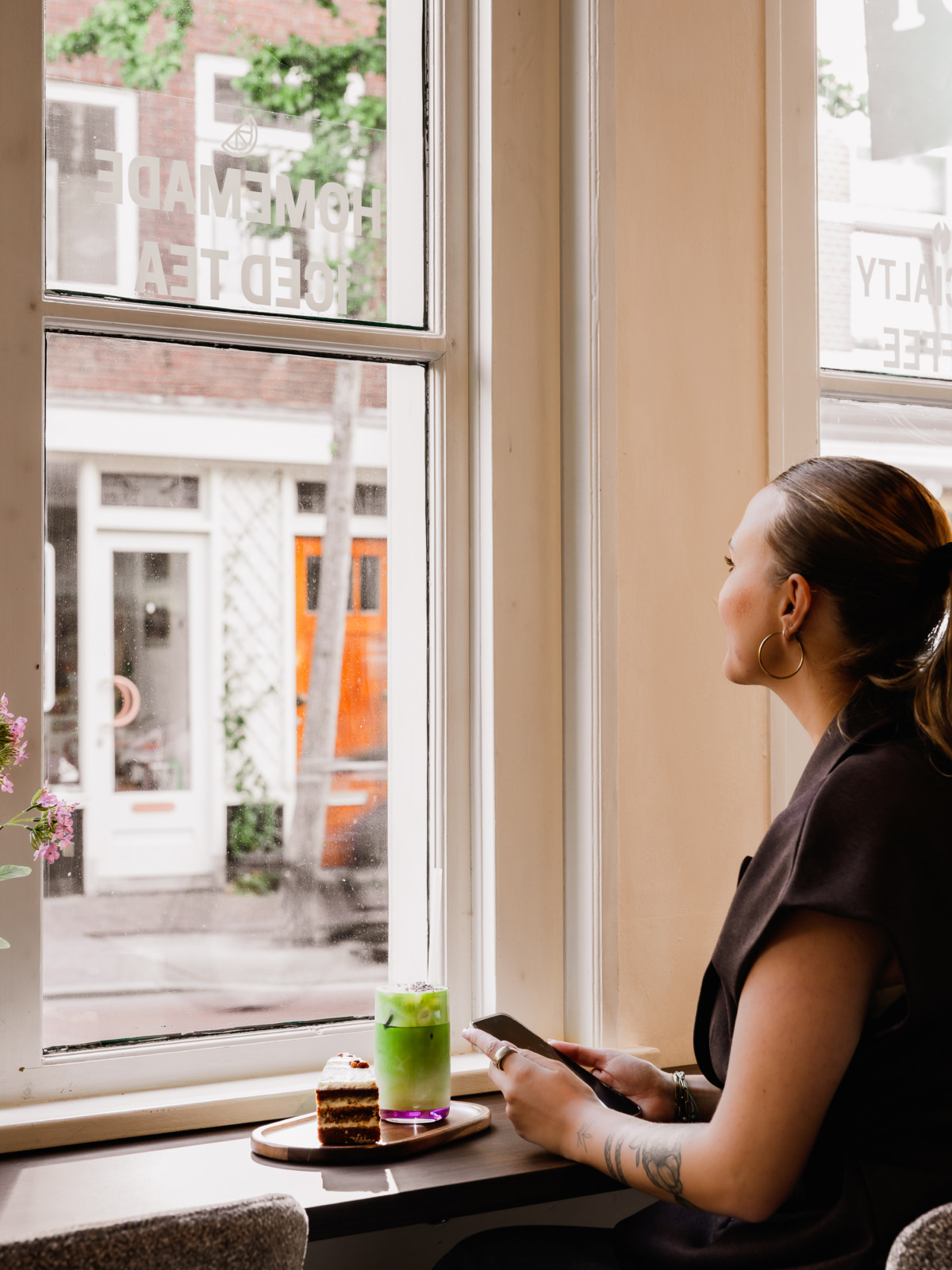 Vrouw bij het raam met een matcha latte en taart in koffiebar Forty Five in Utrecht