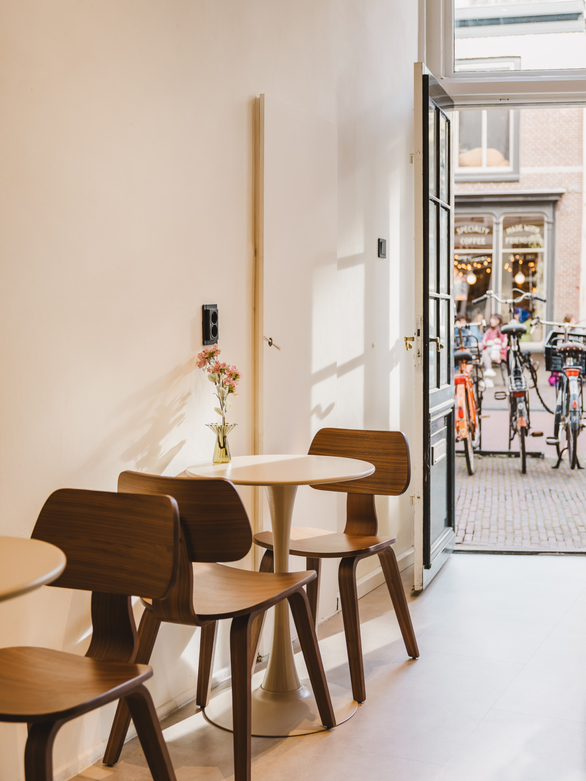 Zithoek met houten stoelen en ronde tafels bij de open deur van koffiebar Forty Five in Utrecht
