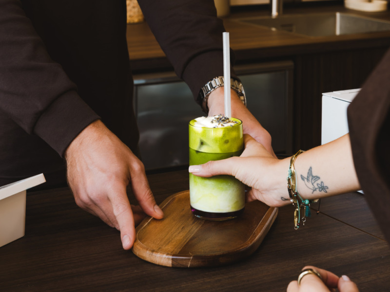 Iced matcha latte wordt over de bar aangereikt in koffiebar Forty Five in Utrecht, zakelijke fotografie